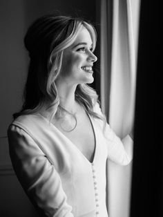 a woman standing next to a window looking out at the outside in black and white