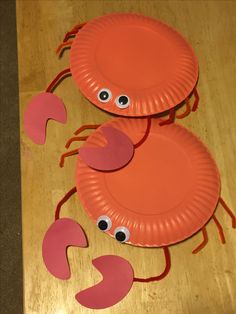 two paper plates with eyes and legs made to look like crabs on a wooden table