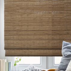 a room with a window covered in bamboo blinds and books on the table next to it