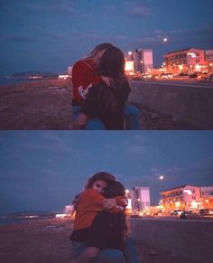 two people hugging each other in front of the ocean at night with city lights behind them