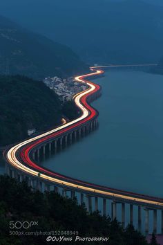 a long exposure shot of a highway going over a bridge at night with the lights on