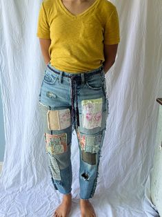 a woman standing in front of a white backdrop wearing blue jeans with patches on them