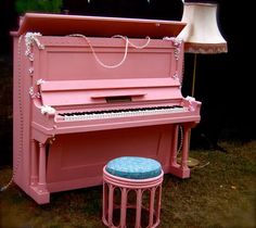 an old pink piano and stool are sitting in front of a lamp on the grass