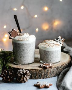 two glasses filled with pudding on top of a wooden board next to christmas decorations and lights