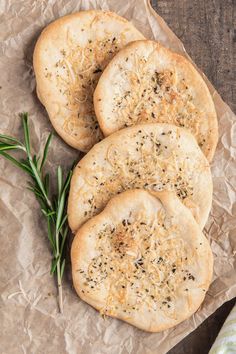 three garlic breads on top of brown paper next to a sprig of rosemary