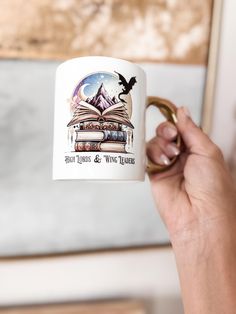 a hand holding a coffee mug with an image of books and a bird on it