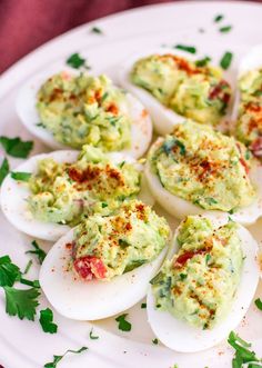 deviled eggs topped with guacamole and parsley on a white plate