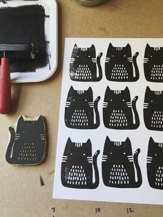 several black cats on white paper next to a rubber stamp and some scissors with red ink