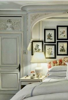 a white bed sitting in a bedroom next to pictures on the wall and lamps above it