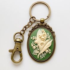 "Lily of the Valley Keychain Cameo Key Chain Floral Accessories -I make these keychains using your choice of Antique Silver or Antique Brass hardware, keychain hook along with a large clasp for clipping onto purses or adding other keychain accessories to; rose cameo is green and cream -Nickel free and lead free alloy metal, resin cameo -Select your finish from the dropdown menu -Measures 3\" long (from top of round keyring to bottom of cameo) x 1 3/8\" wide (cameo width) -Gift Boxed More of my L Antique Keychain, Lily Of The Valley Keychain, Green Keychain, Vintage Keychain, My L, Keychain Hook, Bridesmaid Favors, Vintage Ideas, Keychain Accessories