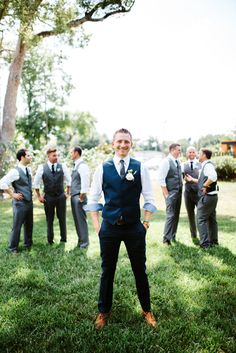 a man standing in the grass with his arms crossed and other men behind him wearing vests