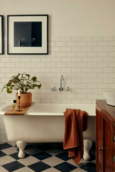 a white bath tub sitting in a bathroom next to a wooden cabinet and framed pictures