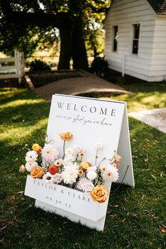 a welcome sign sitting on top of a lush green field next to a white house