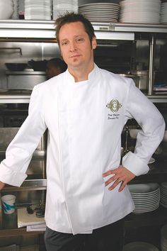 a man in a chef's coat standing next to stacks of plates and bowls