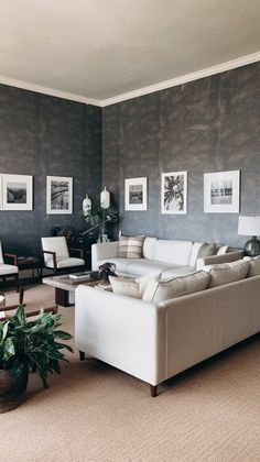 a living room filled with white furniture and pictures on the wall above it's windows