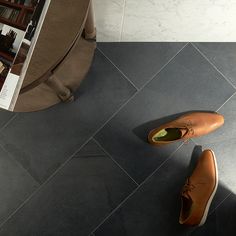 a pair of brown shoes sitting on top of a gray tile floor next to a book shelf