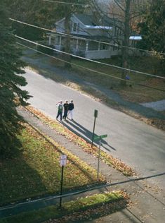 three people are walking down the street in front of some houses and trees, one person is wearing a black jacket