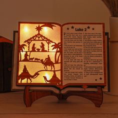 an open book with the nativity scene lit up on it's cover, sitting on a table next to a potted plant