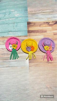 three crocheted flowers sitting on top of a wooden floor next to each other