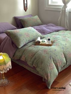 a bed sitting on top of a wooden floor next to a table with a lamp