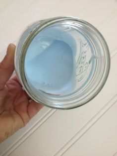 a person is holding a glass jar with blue liquid in it and the lid partially closed