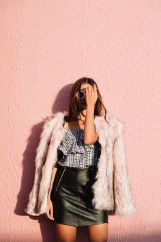 a woman standing in front of a pink wall wearing a black leather skirt and white fur coat