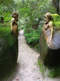 two statues sitting on top of large rocks in the woods