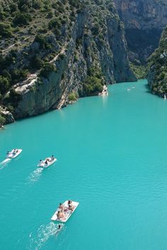 two boats are traveling down the river in front of some rocky cliffs and cliffs