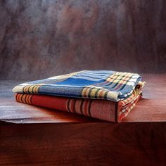 three different colored blankets sitting on top of a wooden table next to a brown wall