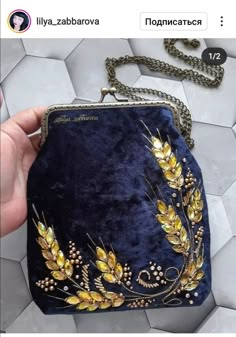 a hand holding a blue velvet purse with gold leaves on the front and side,