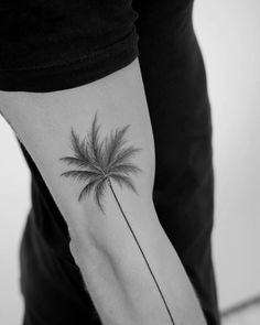 a black and white photo of a palm tree tattoo on the left inner arm,