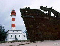 an old rusted boat sitting next to a light house with a red and white lighthouse in the background