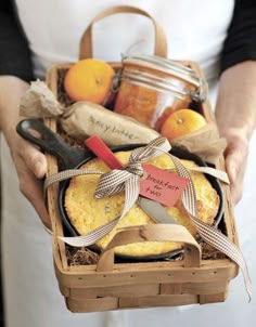 a person holding a basket filled with bread and oranges next to some jam jars