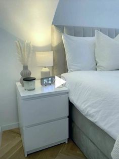 a white bed sitting next to a night stand with an alarm clock on top of it