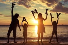 a family standing on the beach with their arms in the air and letters spelling out