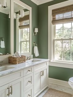 a bathroom with green walls, white cabinets and two sinks in the middle of it