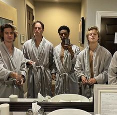 four men in robes taking a selfie in front of a bathroom mirror with the reflection of them