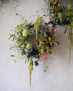 an arrangement of green and blue flowers on a white wall with greenery hanging from it's sides