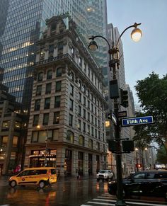 a yellow taxi cab driving down a street next to tall buildings and traffic lights on a rainy day