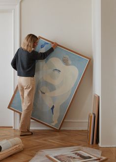 a woman standing in front of a painting on the wall holding it up to her face