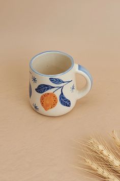 a blue and white coffee cup sitting on top of a table next to some wheat