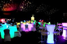 a room filled with lots of tables and chairs covered in bright colored lights at night