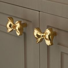 two gold bow knobs on the front of a white cabinet