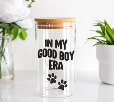 a glass jar with the words in my good boy era on it next to a potted plant