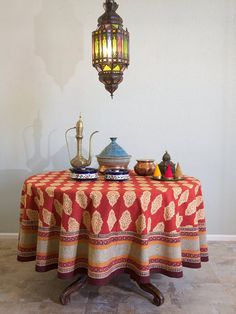 a table topped with a red and gold cloth covered table next to a light fixture