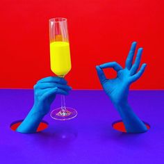 two hands in blue gloves holding up a wine glass with yellow liquid on the bottom