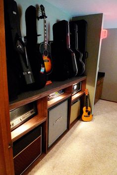 guitars and amps are lined up against the wall in this room with carpeted flooring