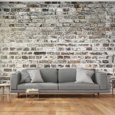 a grey couch sitting on top of a wooden floor next to a white brick wall