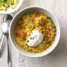 two bowls filled with soup and vegetables on top of a white table cloth next to silver spoons