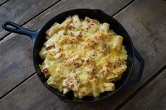 a skillet filled with macaroni and cheese on top of a wooden table